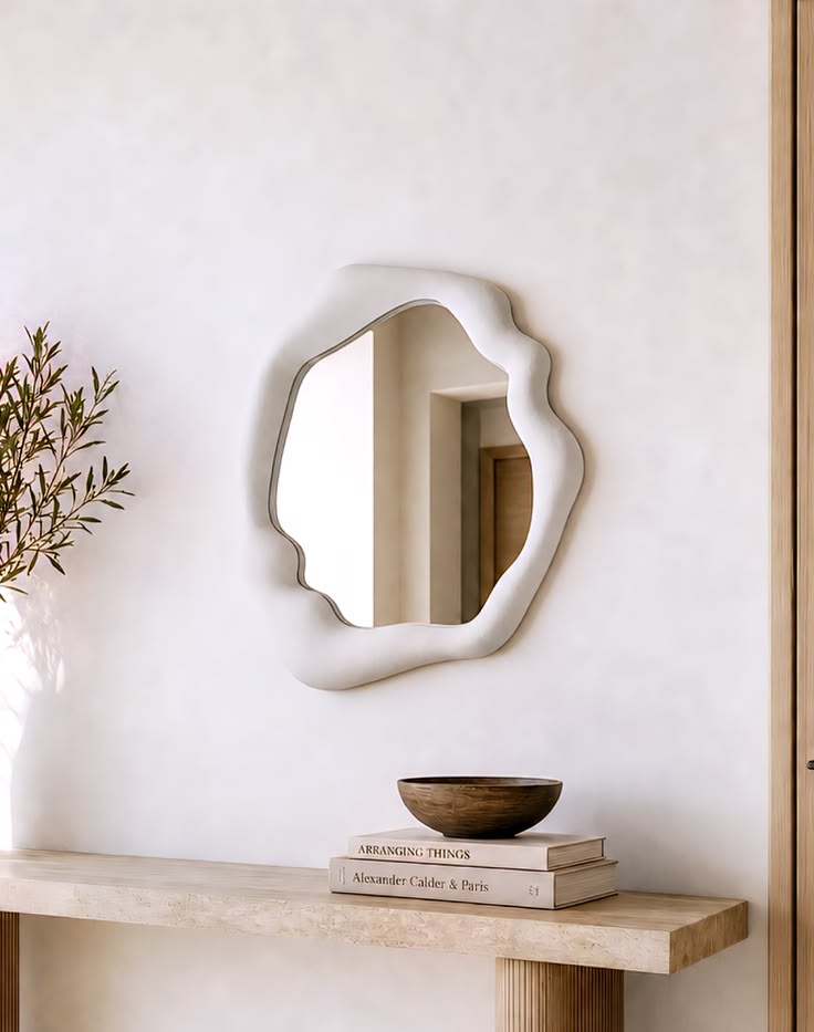 Haven organic modern amorphous wall mirror with a thick cream bouclé frame hanging above a light wood console table.
