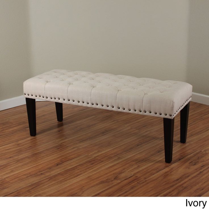 Classic rectangular bench with ivory linen button-tufted upholstery and black tapered wooden legs featuring a brass nailhead trim profile.