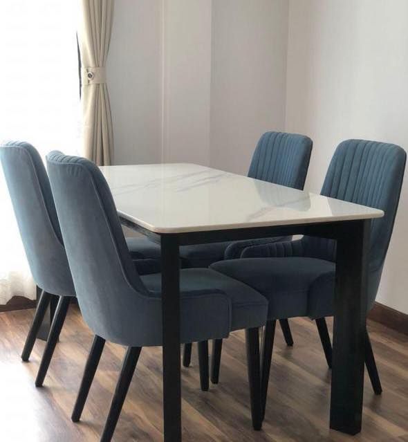 modern 5-piece dining room set showcasing a glossy white faux marble top table with black metal legs surrounded by four dusty blue velvet upholstered chairs with vertical tufting.