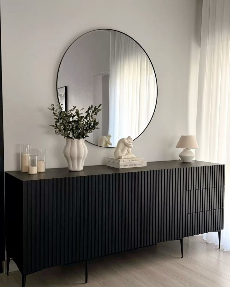 Contemporary Ethnicraft Roller Max sideboard in off-black with a fluted wood-stick pattern, styled with an organic cream vase, stacked books, and a lamp beneath a round black mirror.