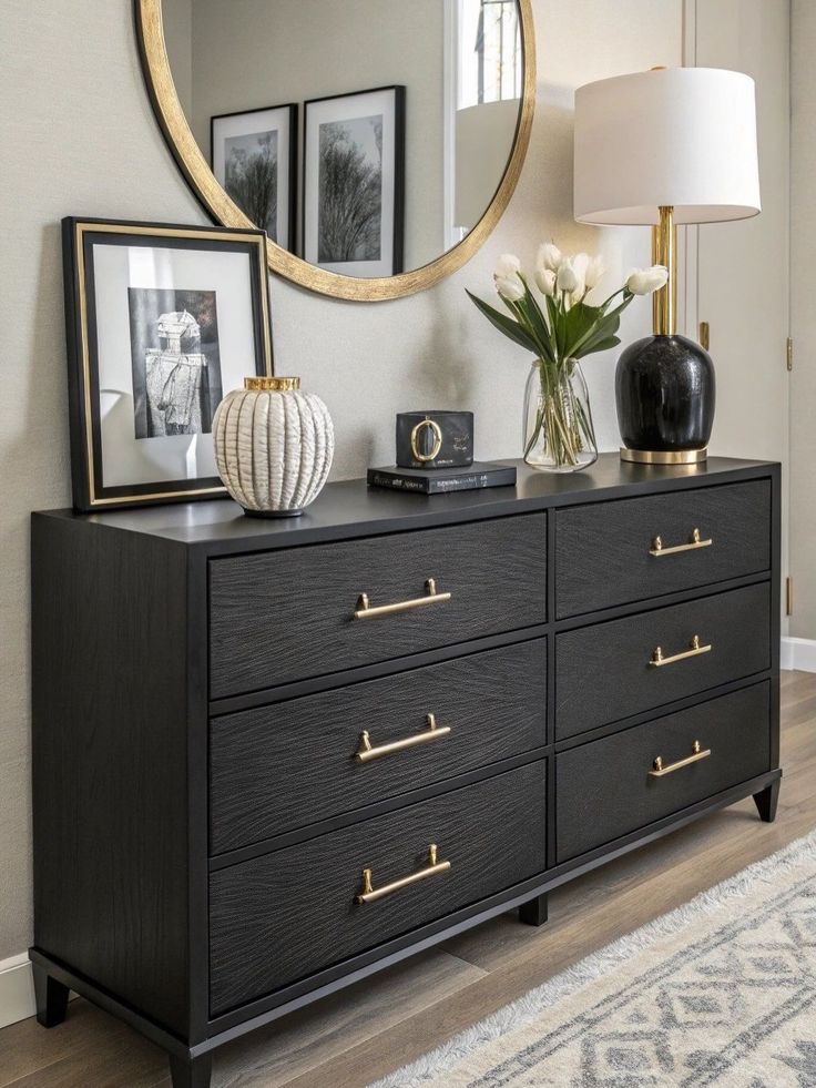 A contemporary matte black oak 6-drawer double dresser styled with elegant gold T-bar handles, featuring a table lamp and decor beneath a round gold mirror.