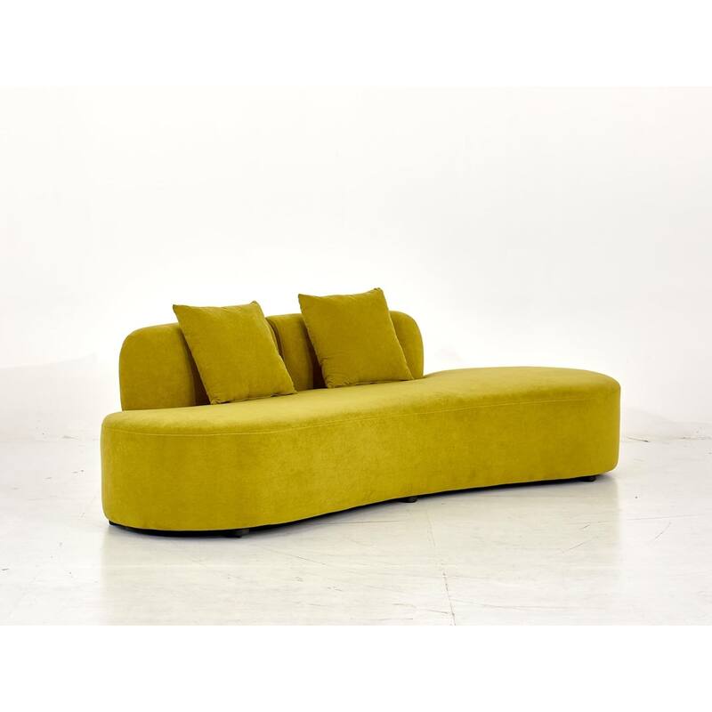 A post-modern asymmetrical curved sofa upholstered in chartreuse olive velvet with two matching throw pillows against a clean white background.