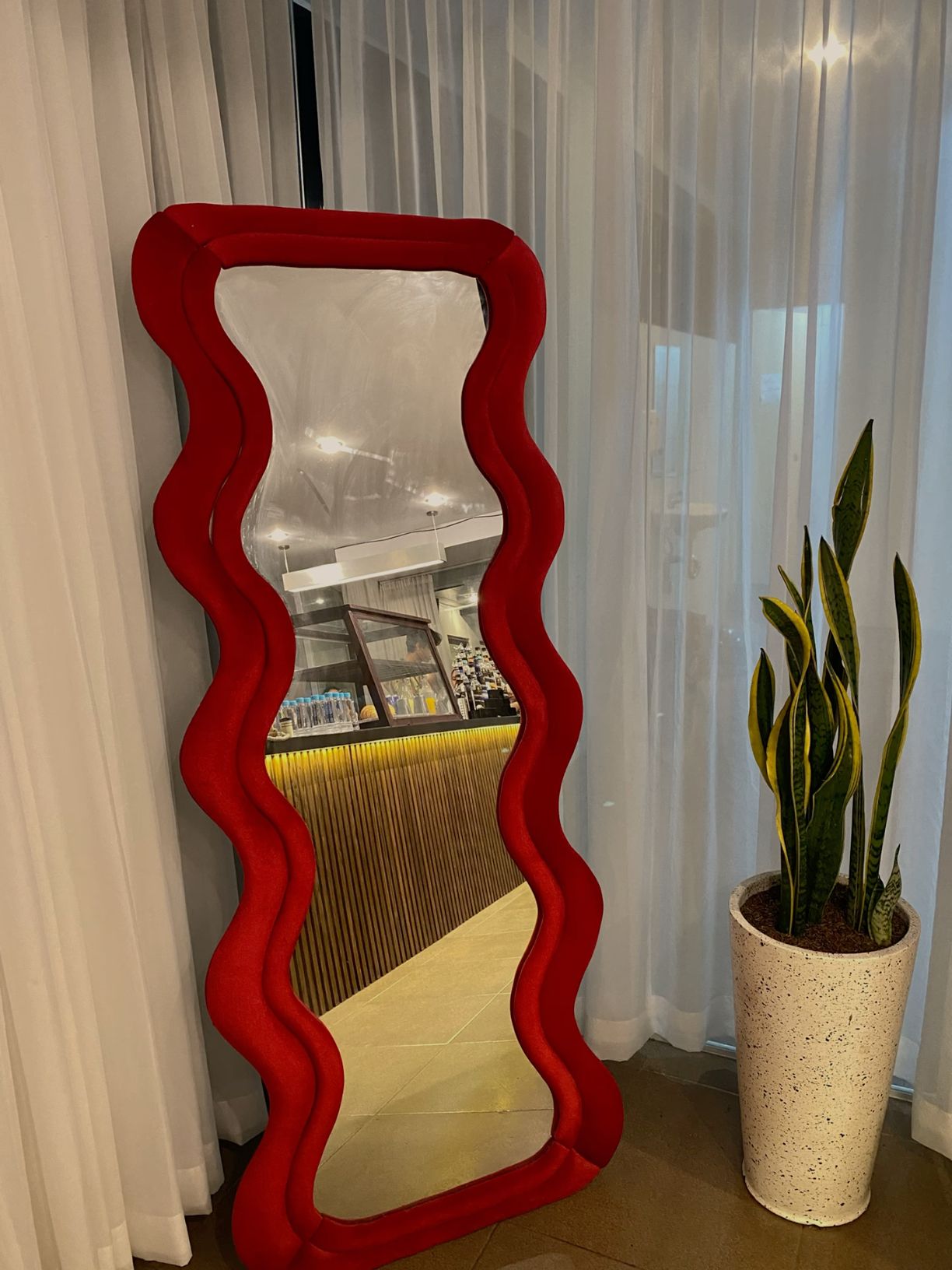 Roxie postmodern full-length floor mirror featuring a bold red velvet wavy frame styled next to a tall snake plant.