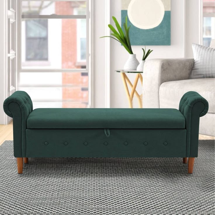 A button-tufted teal velvet storage bench with rolled arms and light wood legs placed on a geometric gray rug in a modern living room setting.