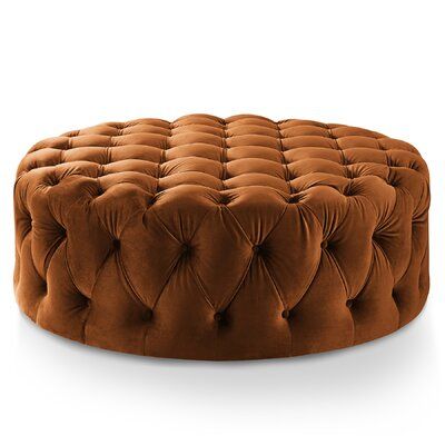 Large round performance velvet ottoman with all-over deep button tufting in cognac brown against a white studio backdrop.