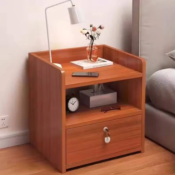 Walnut wooden bedside table sitting next to a bed, showcasing an open storage shelf with a tissue box and clock, and a bottom locked drawer with keys.